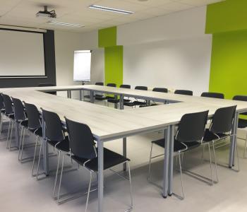 photo of a conference room with black chairs around a big table and a projector screen at the further end